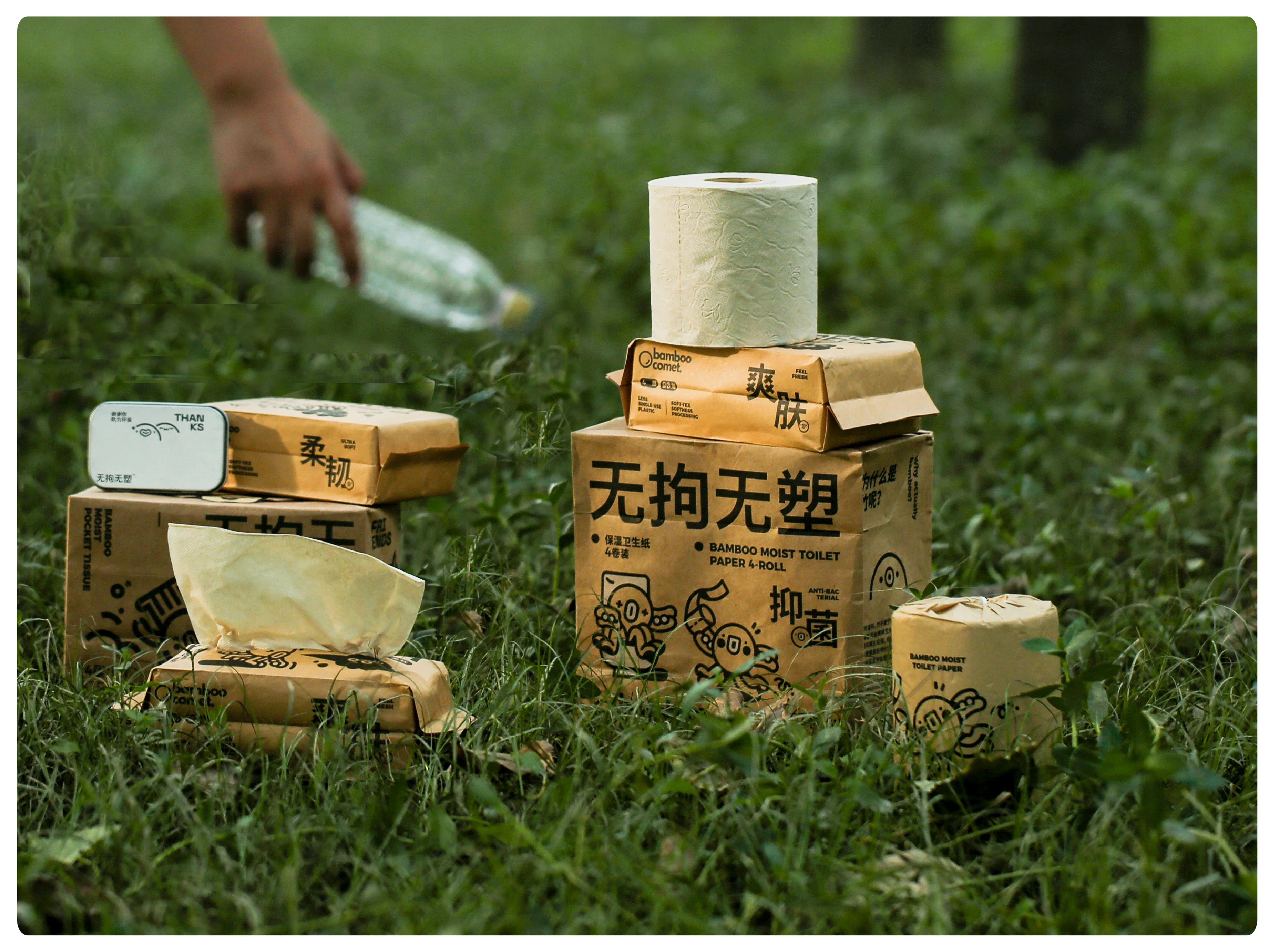 草地上陈列的 BambooComet 纸巾包装、卷纸与纸巾盒